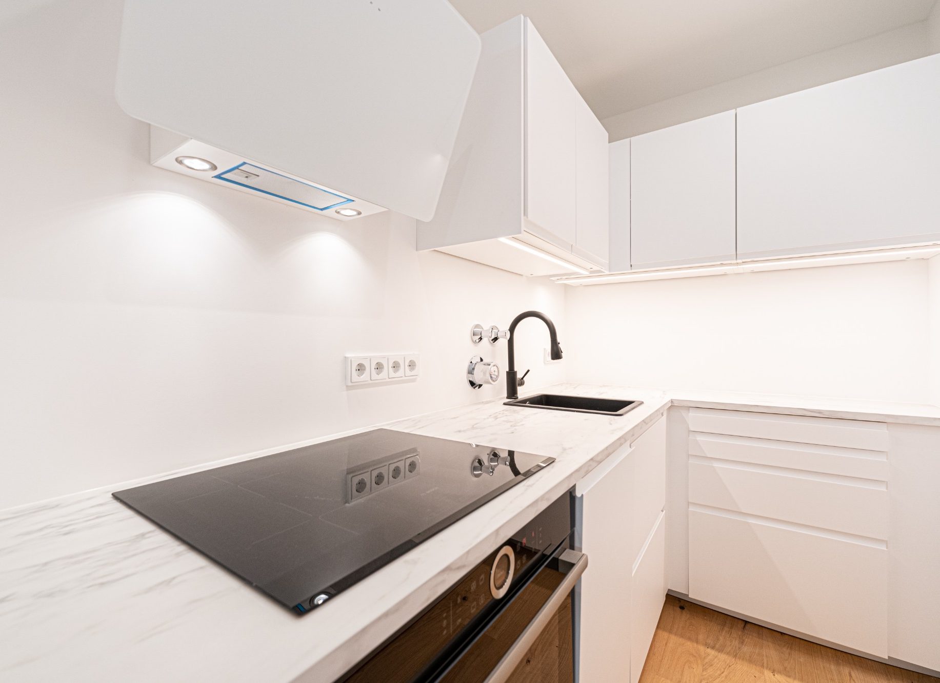 Wohnungssanierung München moderne Küche mit Marmorarbeitsplatte, Einbaugeräten und schwarzen Details